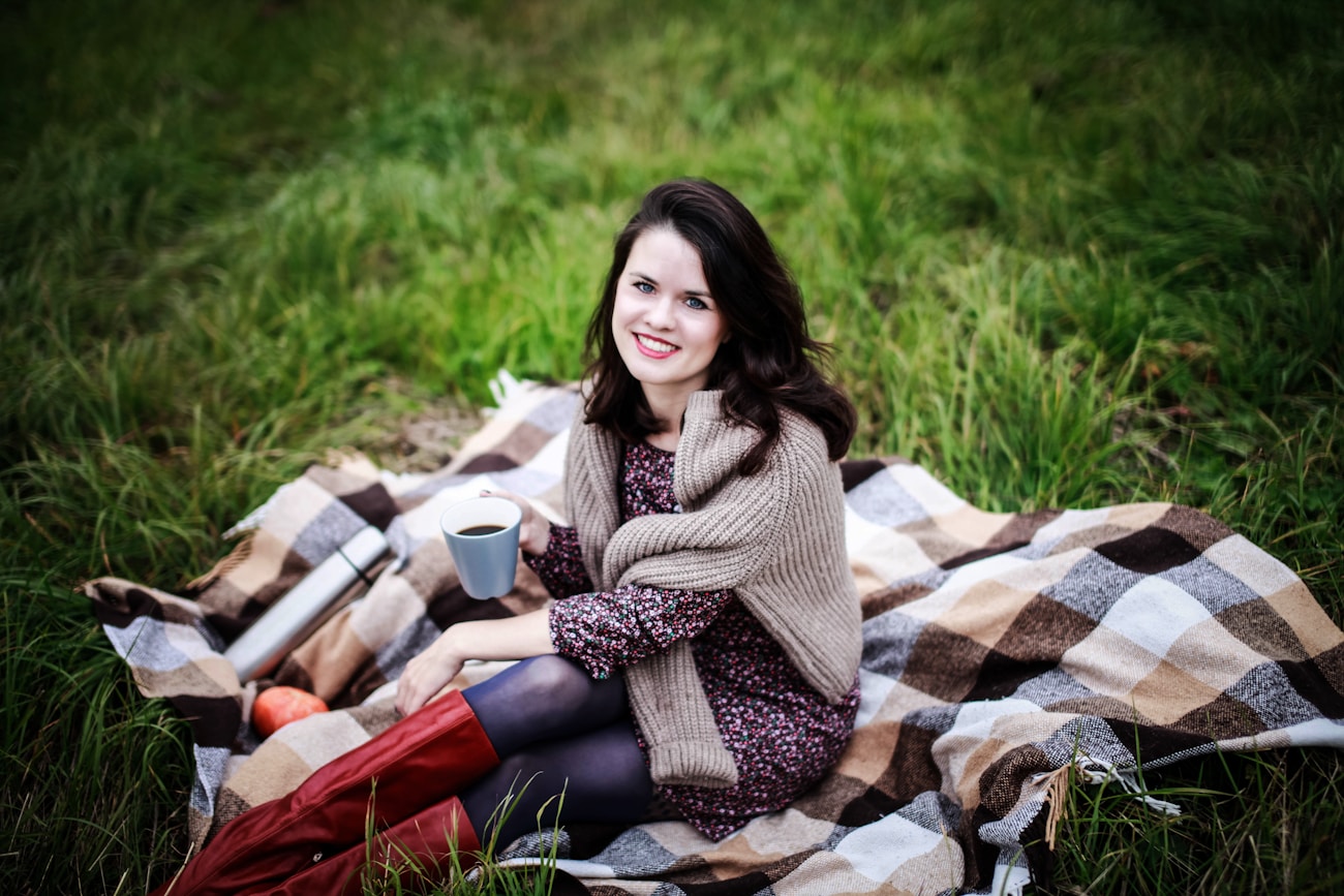 Woman sitting on a cozy blanket outdoors with coffee for a relaxed portrait