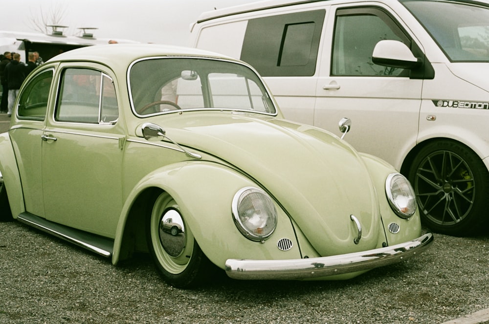 a green vw bug parked next to a white van