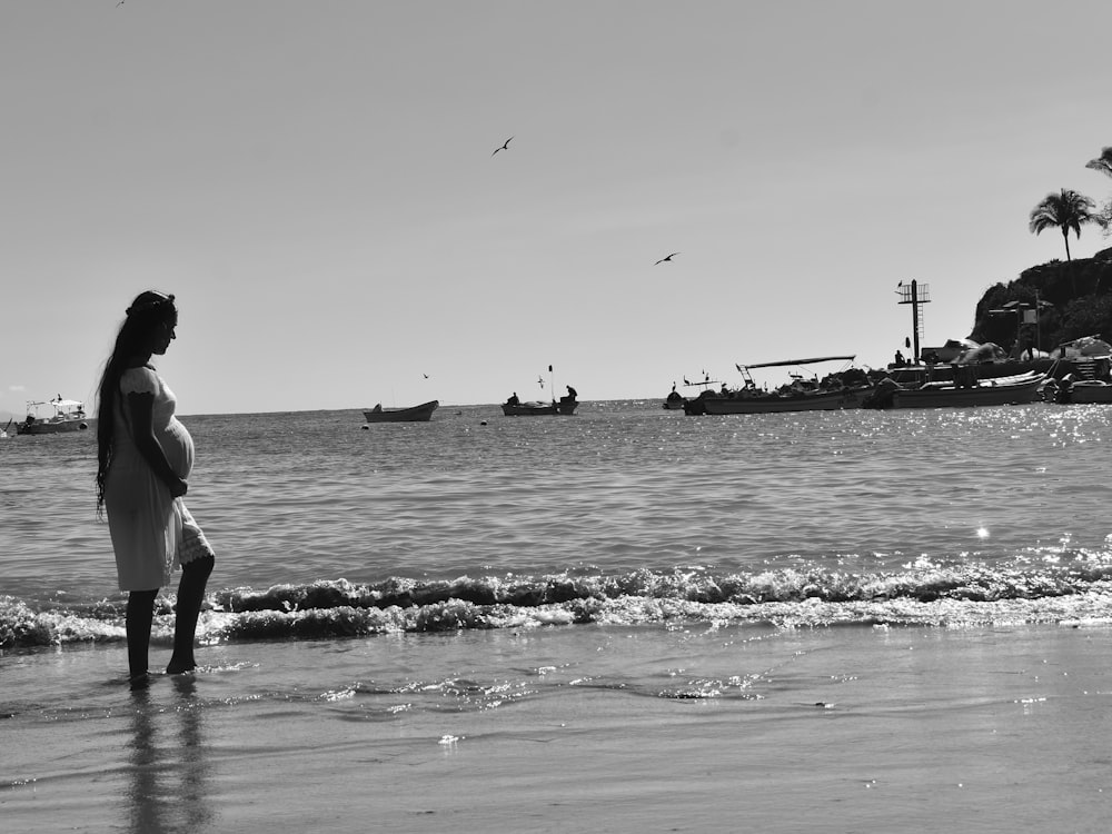 a pregnant woman standing on a beach next to the ocean