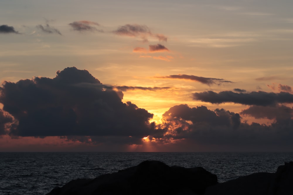 the sun is setting over the ocean with clouds