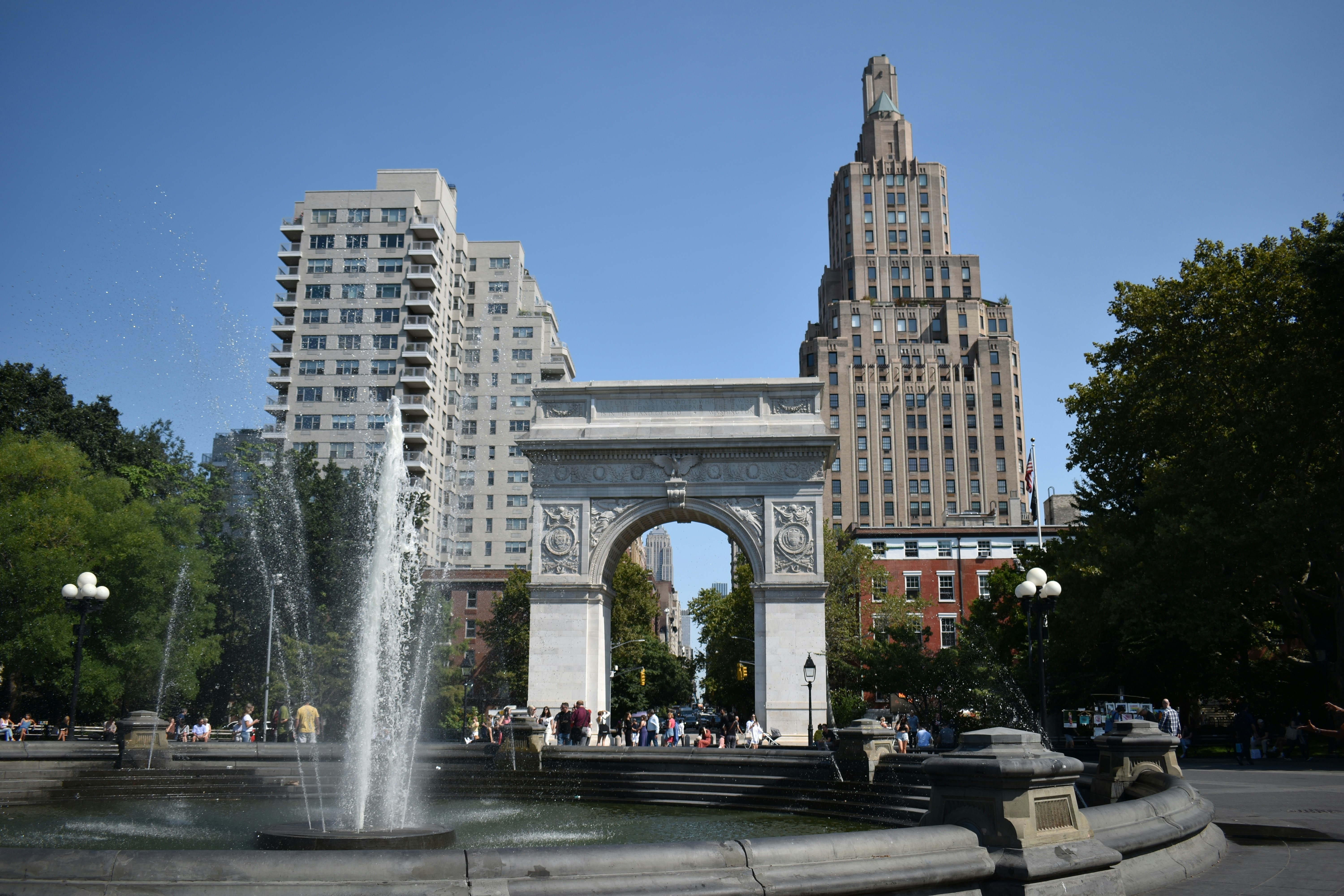 Iconic Washington Square Arch in Greenwich Village, New York City, surrounded by park greenery and city buildings — a symbol of the neighborhood marketed by The Parviz Team at Compass.