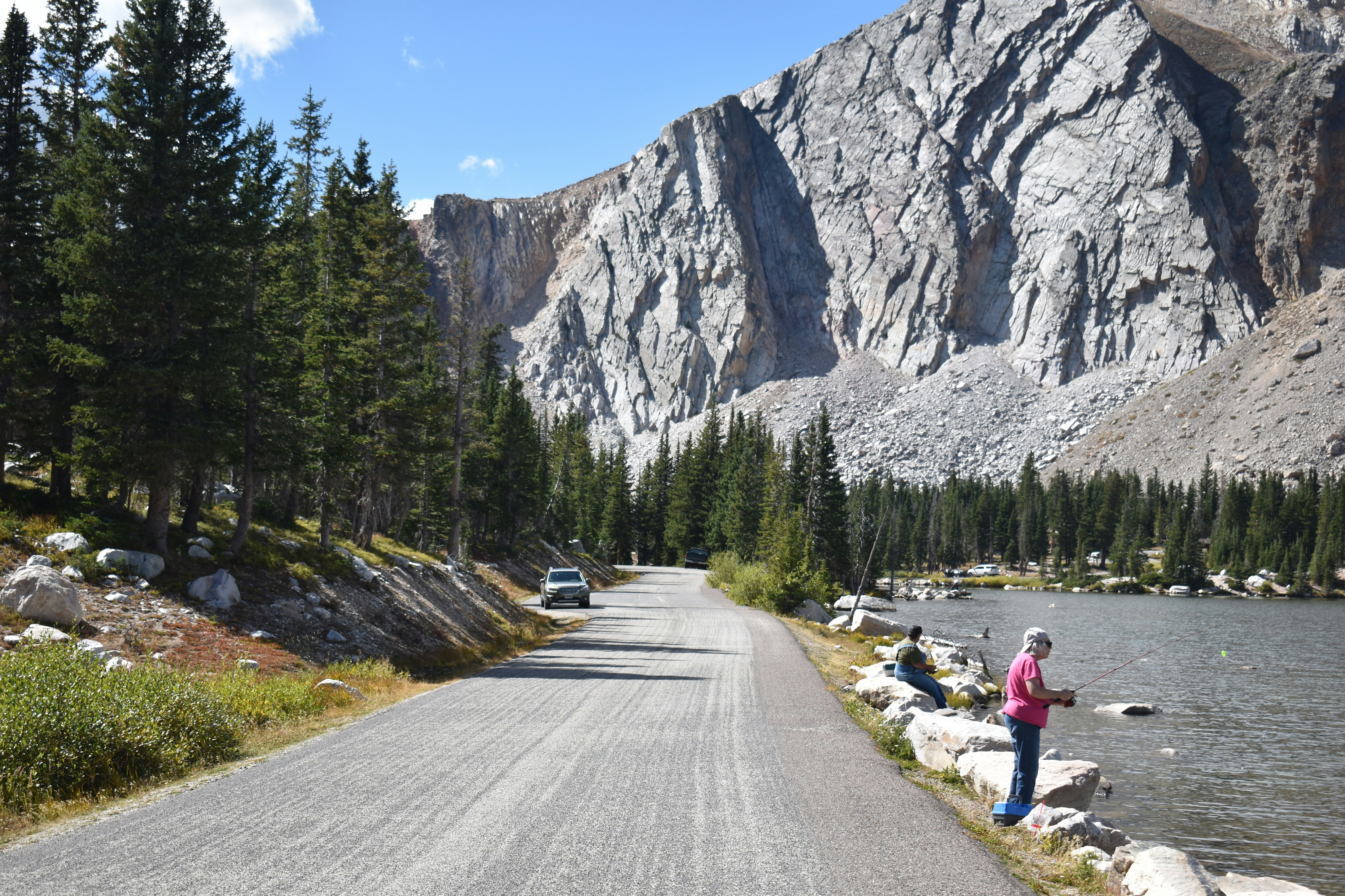 a woman standing on the side of a road next to a lake