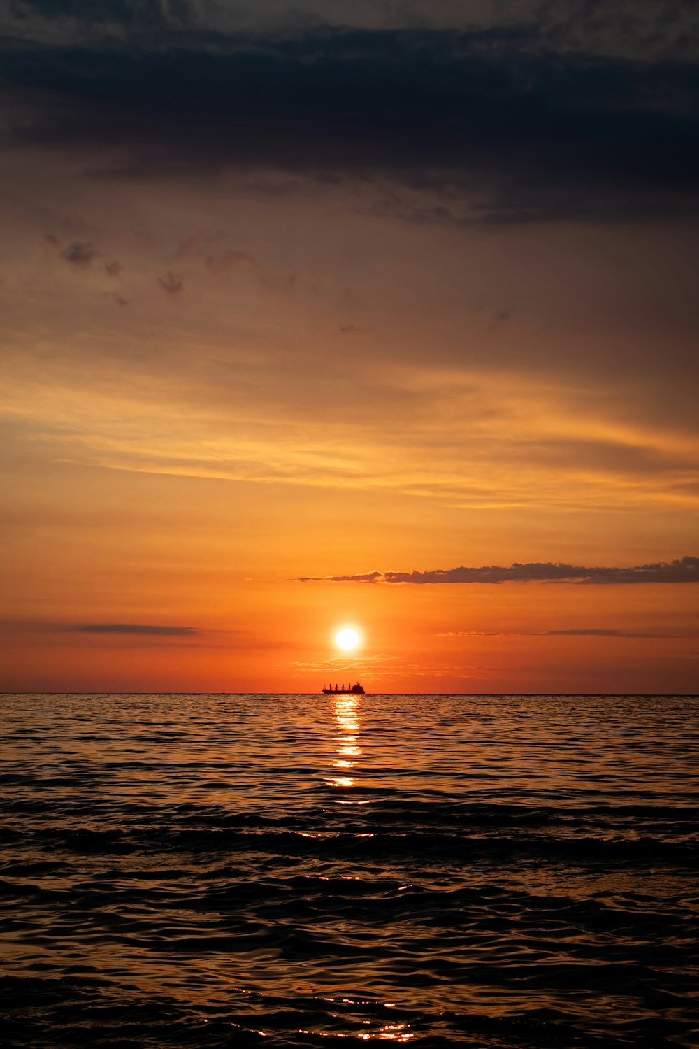 the sun is setting over the ocean with a boat in the distance