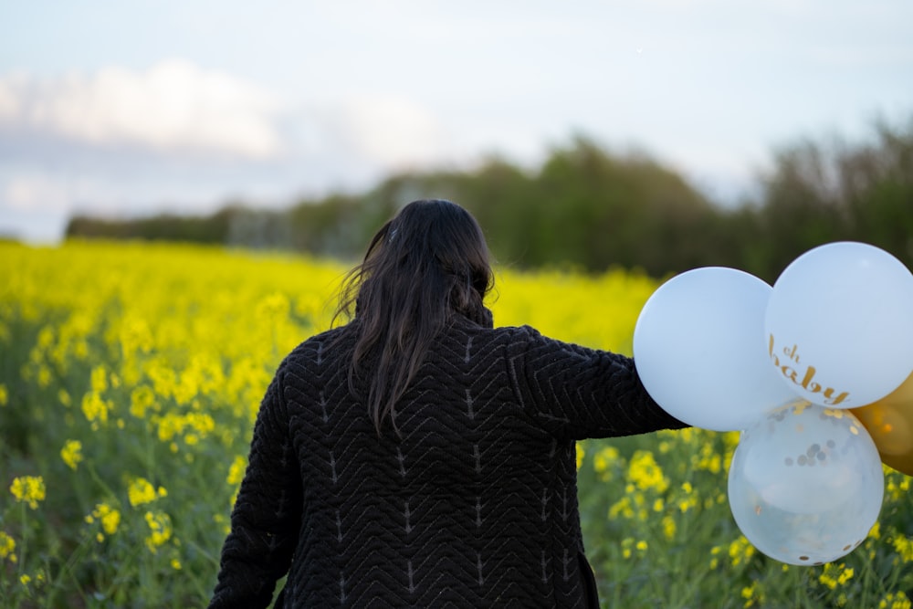 a woman holding a bunch of balloons in a field