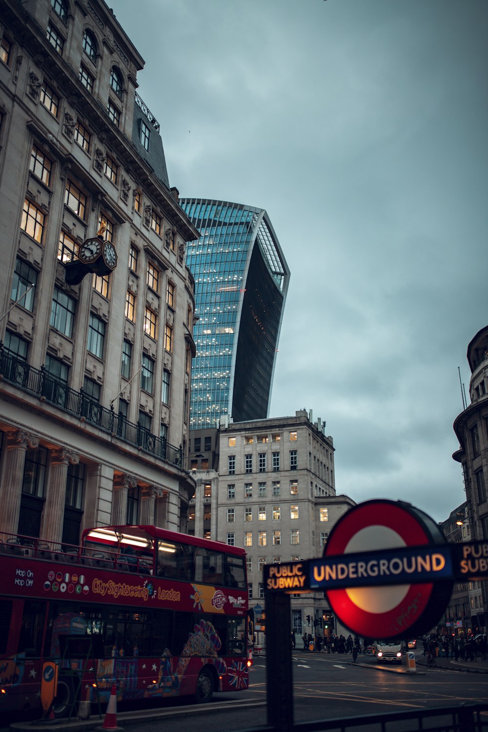 a red double decker bus driving past tall buildings