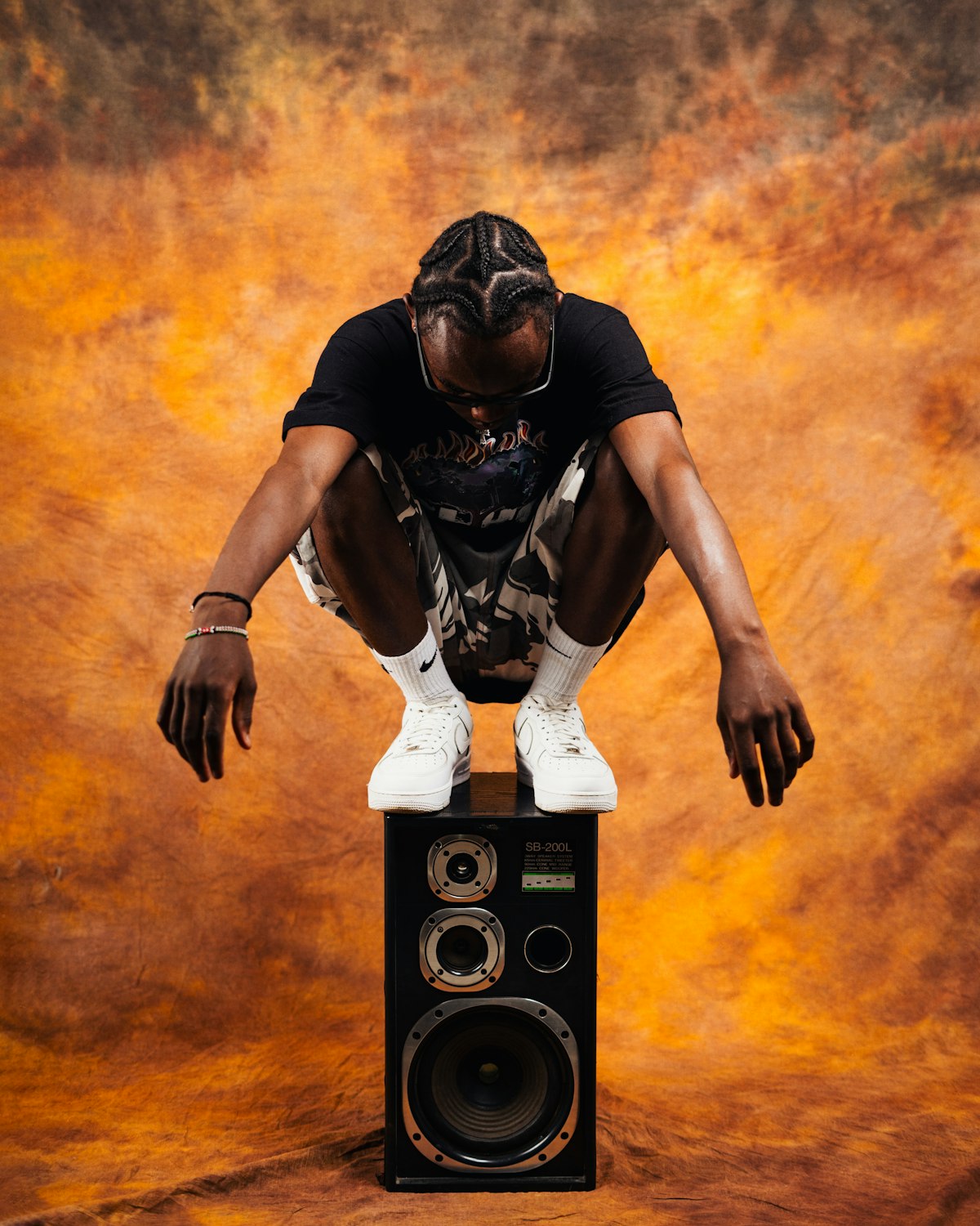 A man crouched on top of a floor speaker in orange smoke