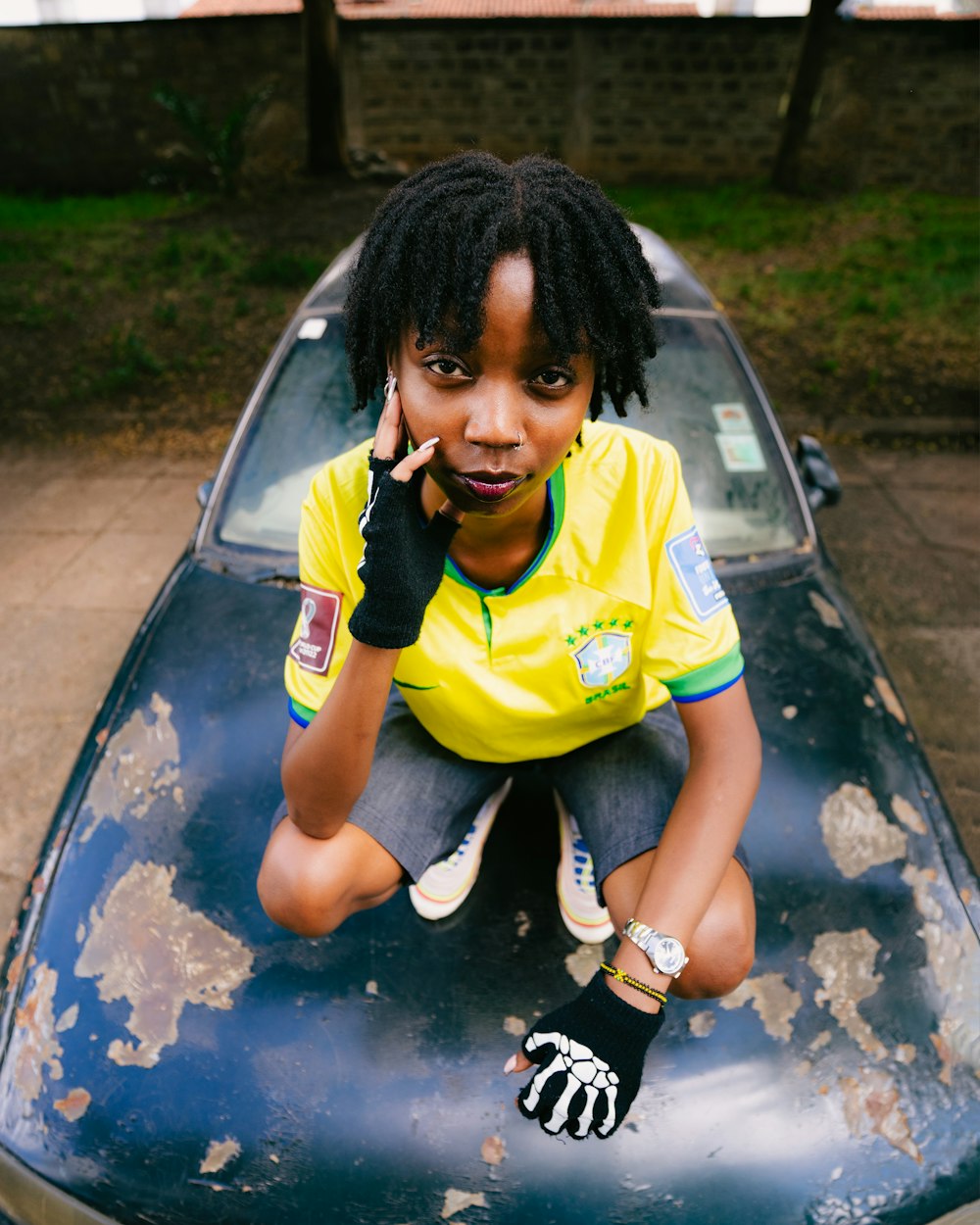 a girl sitting on the hood of a car talking on a cell phone