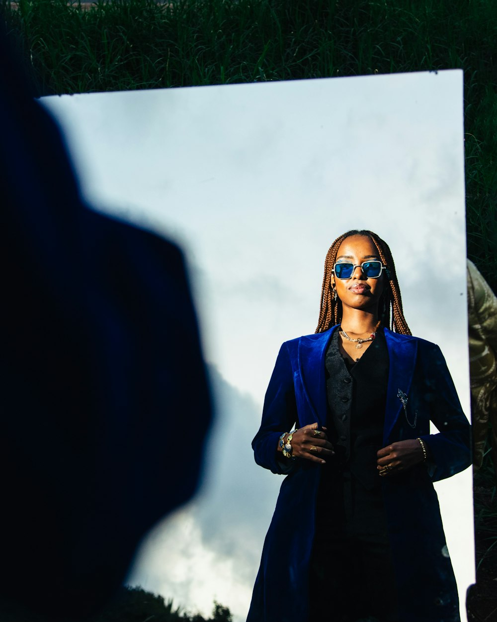 a woman in a blue jacket and sunglasses standing in front of a mirror