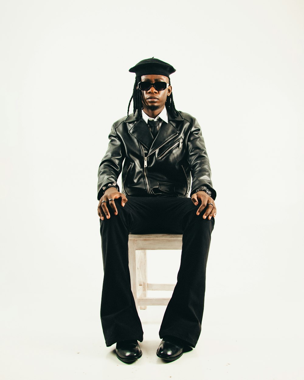 a man in a leather jacket and hat sitting on a stool