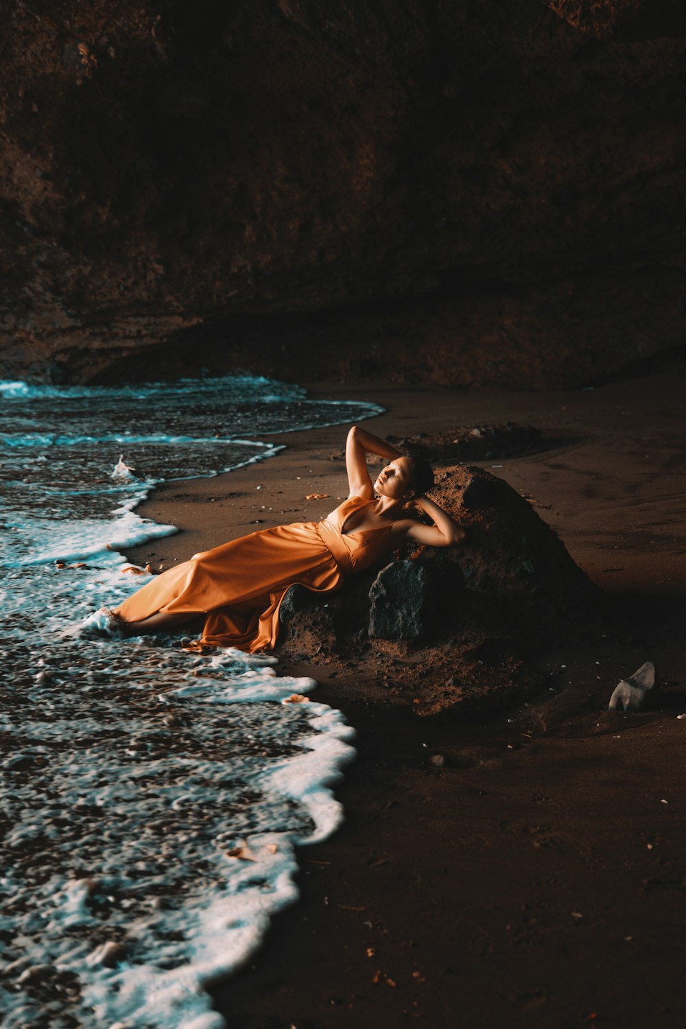 a woman laying on top of a rock near the ocean