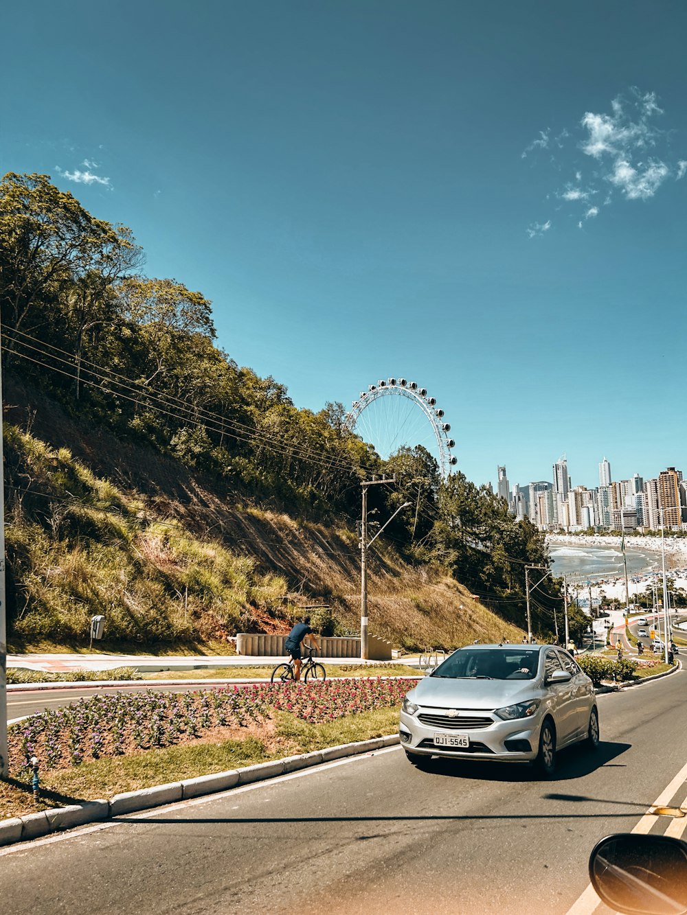 a silver car driving down a street next to a lush green hillside