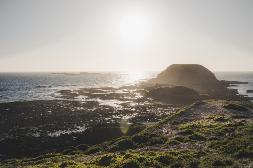 the sun is shining over the ocean and a rock outcropping