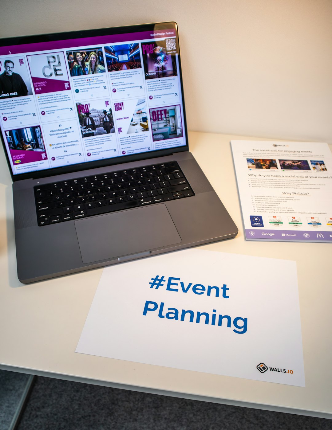 A desk with an event flyer, a piece of paper with the hashtag #EventPlanning and a laptop showing a social media wall