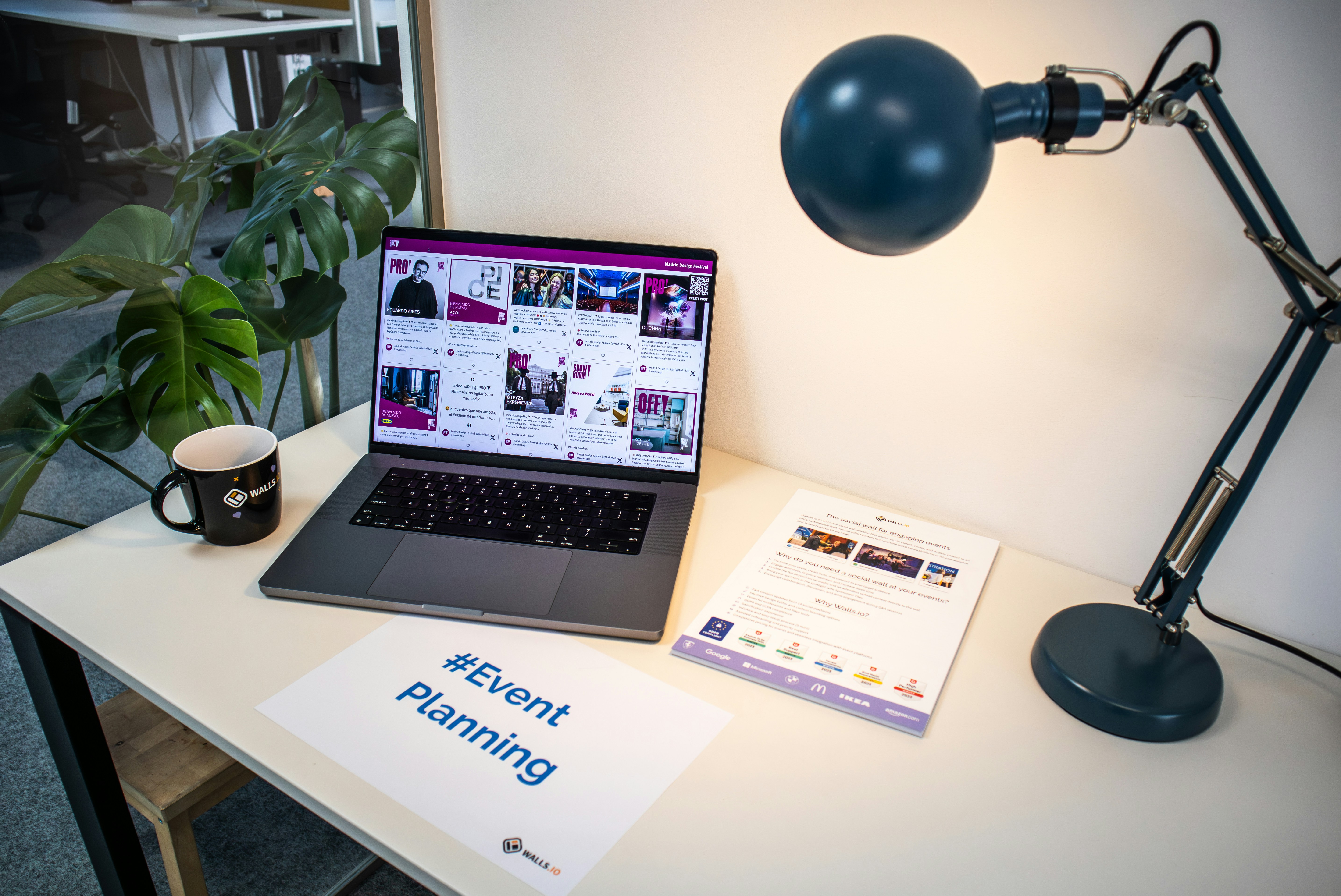 A desk with an event flyer, a piece of paper with the hashtag #EventPlanning and a laptop showing a social media wall