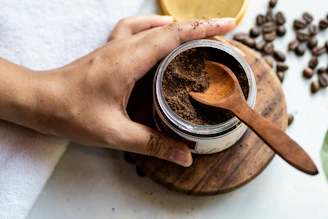 a person holding a wooden spoon over a jar of coffee