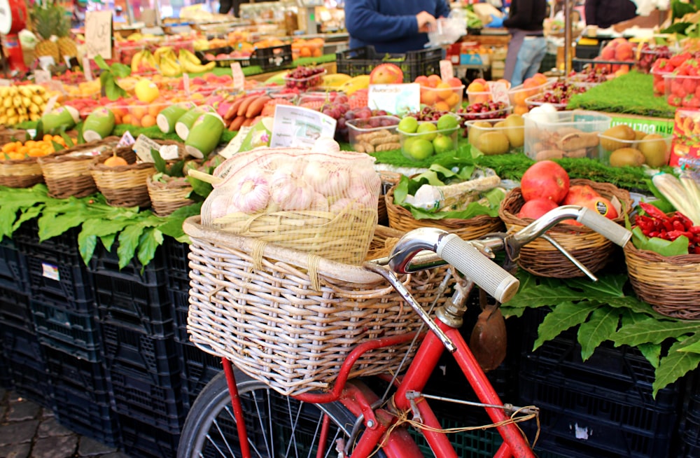 a red bike parked next to a display of fruits and vegetables