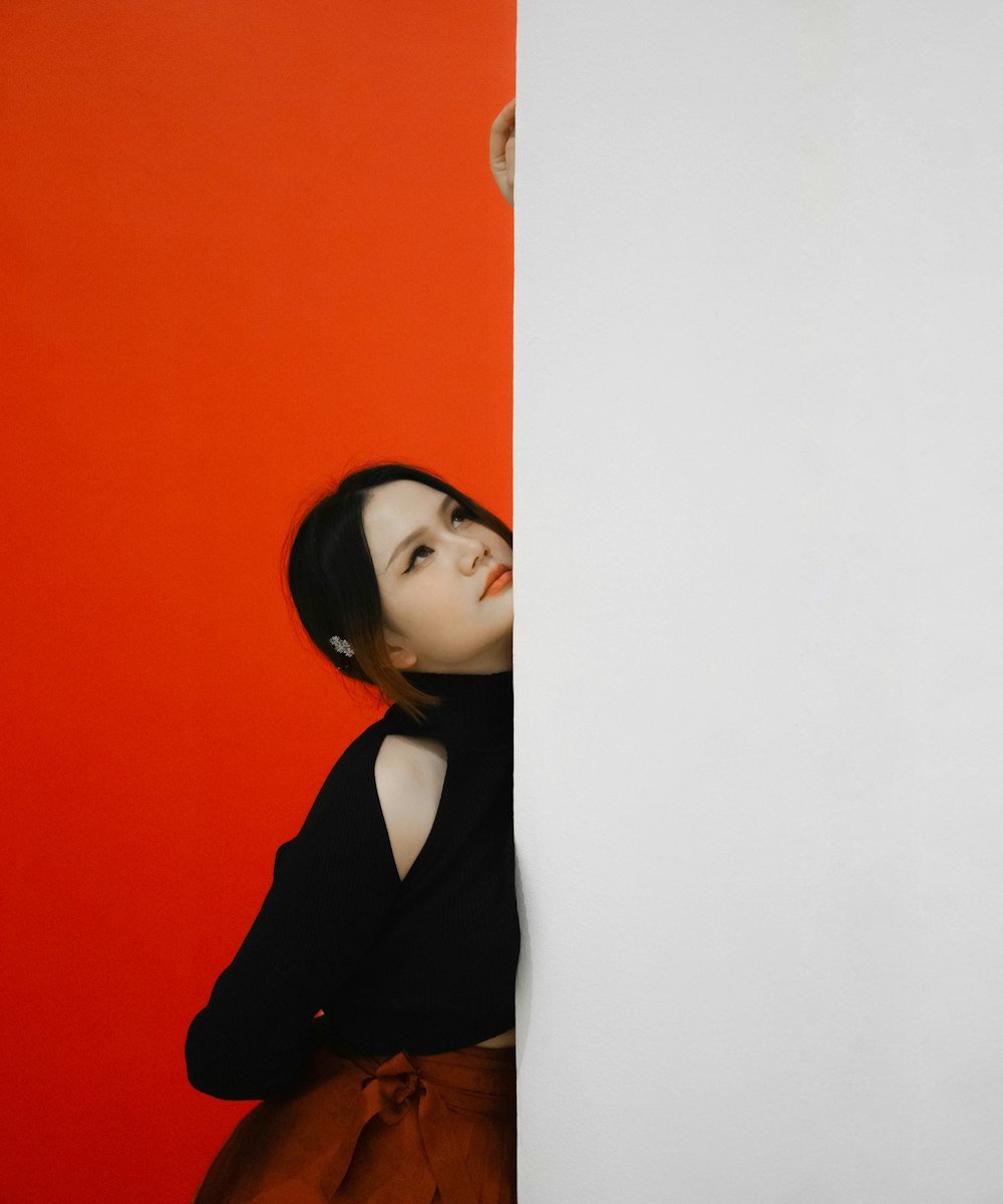 a woman leaning against a wall with a red background