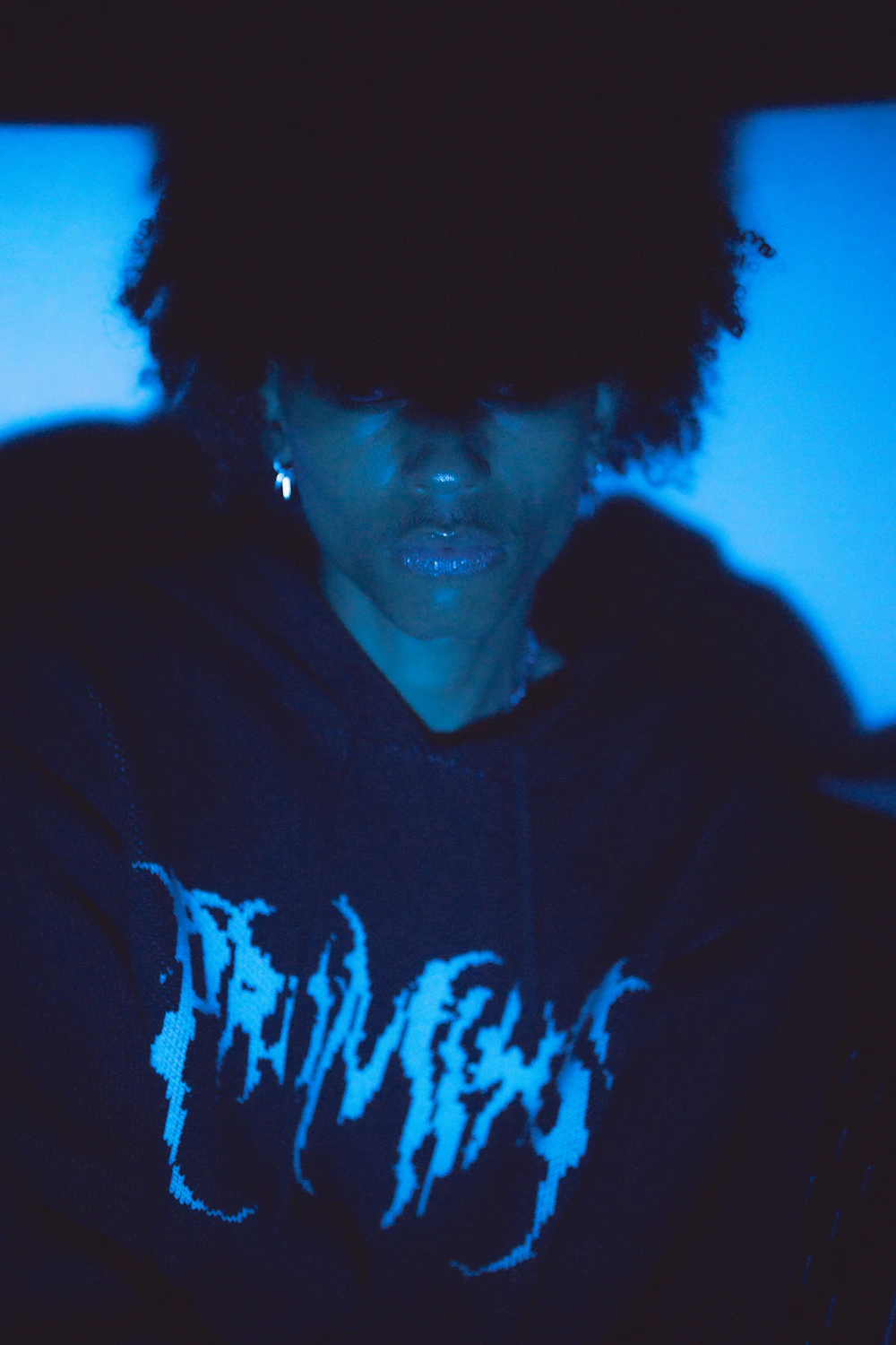 Modelo com moletom preto em fundo azul, estética Y2K