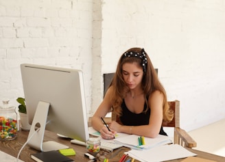 a woman sitting at a desk writing on a piece of paper