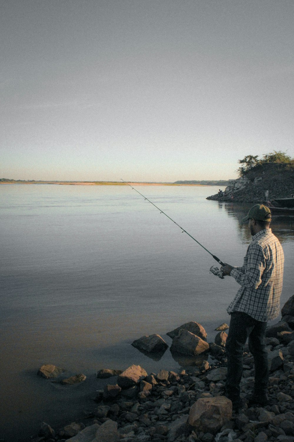 a man standing on a rocky shore while holding a fishing pole