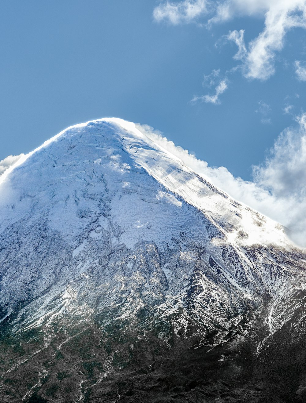 a very tall snow covered mountain under a blue sky