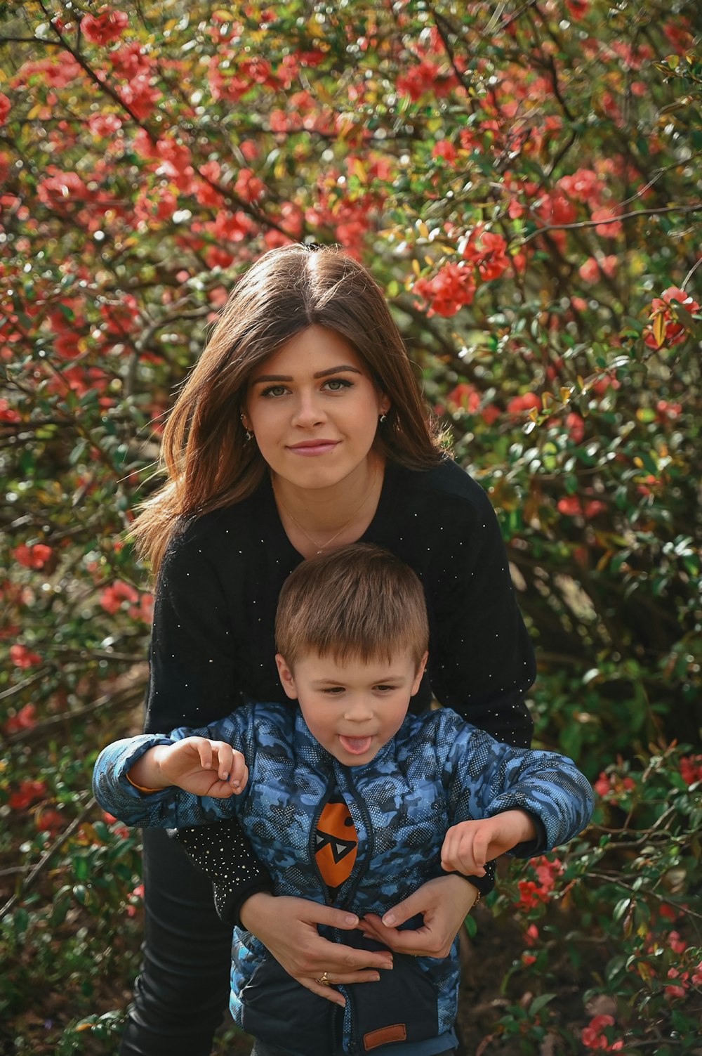 a woman holding a boy in front of a bush