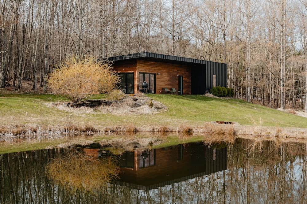 a small cabin sits on a grassy hill next to a body of water