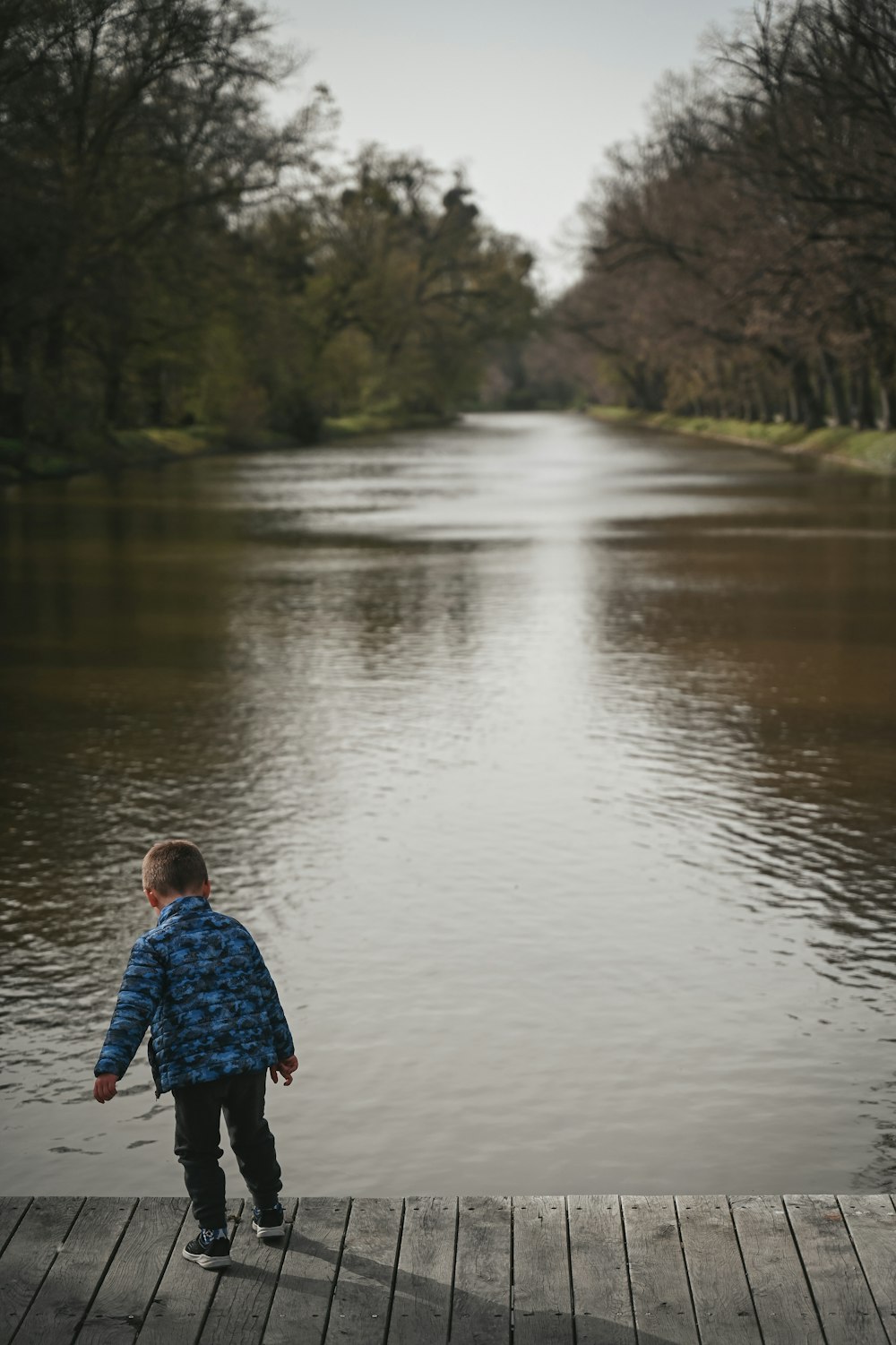 a young boy standing on a dock near a body of water