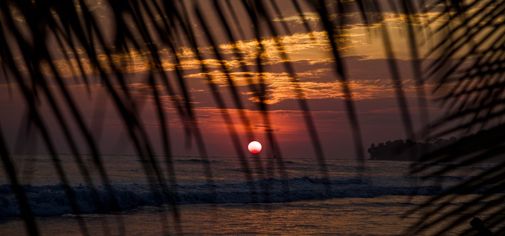 the sun is setting over the ocean on a beach