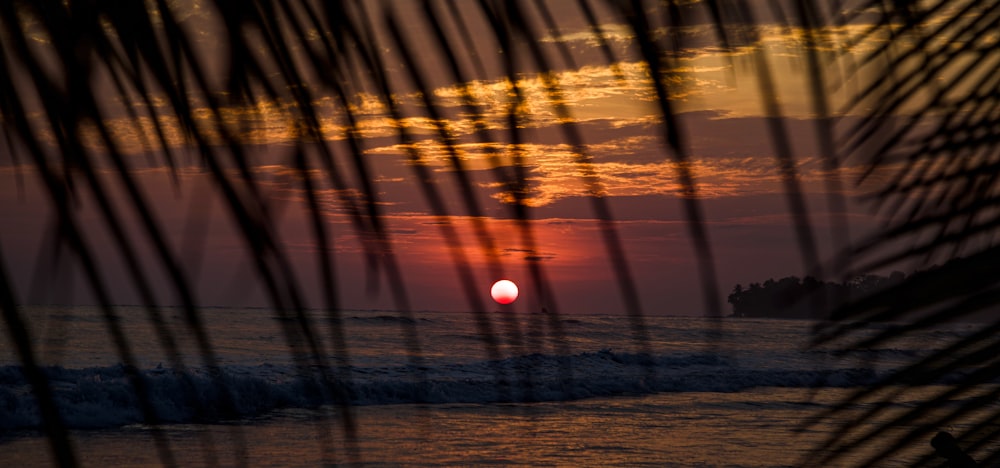 el sol se está poniendo sobre el océano en una playa