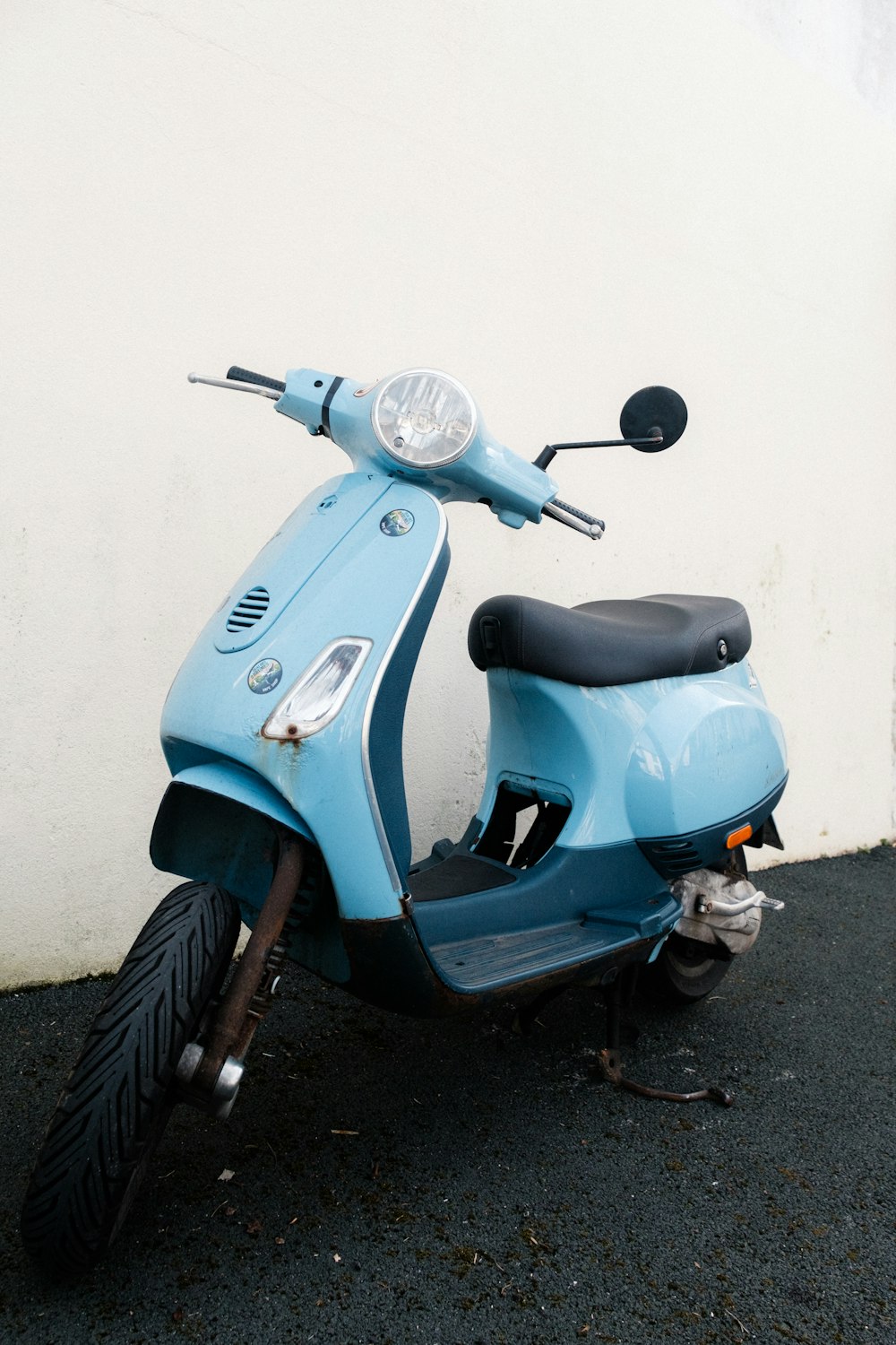 a blue scooter parked next to a white wall