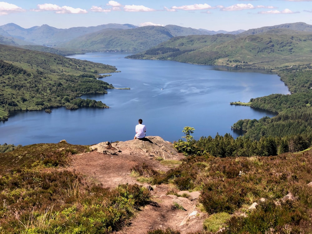 a man sitting on top of a mountain overlooking a lake