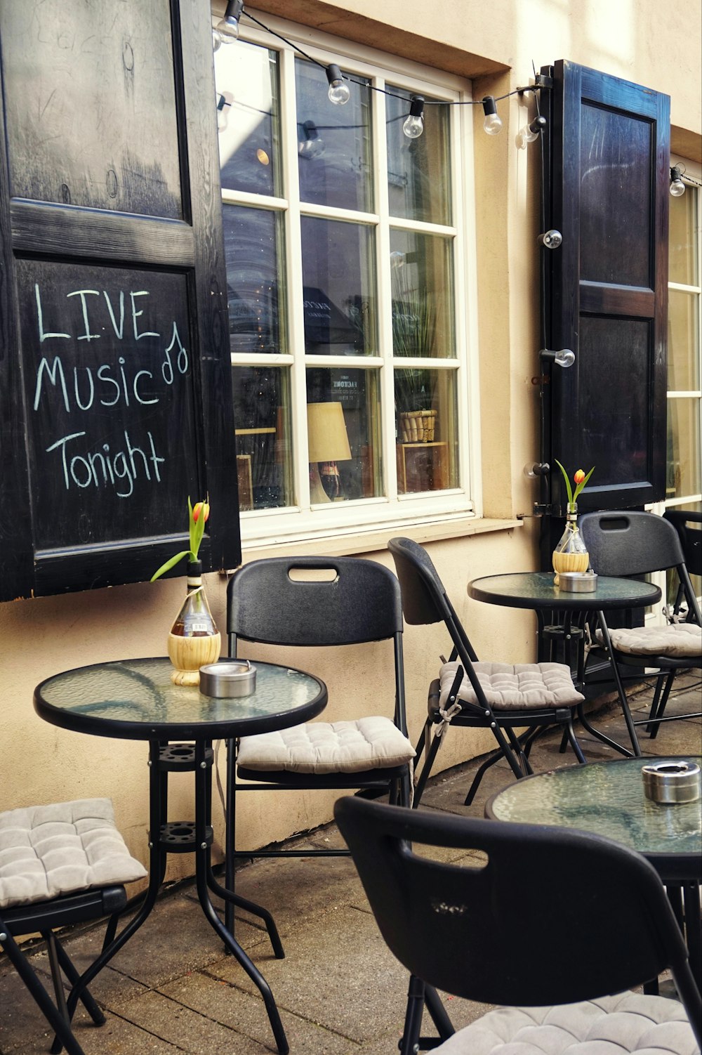 tables and chairs outside of a restaurant with a chalkboard on the wall