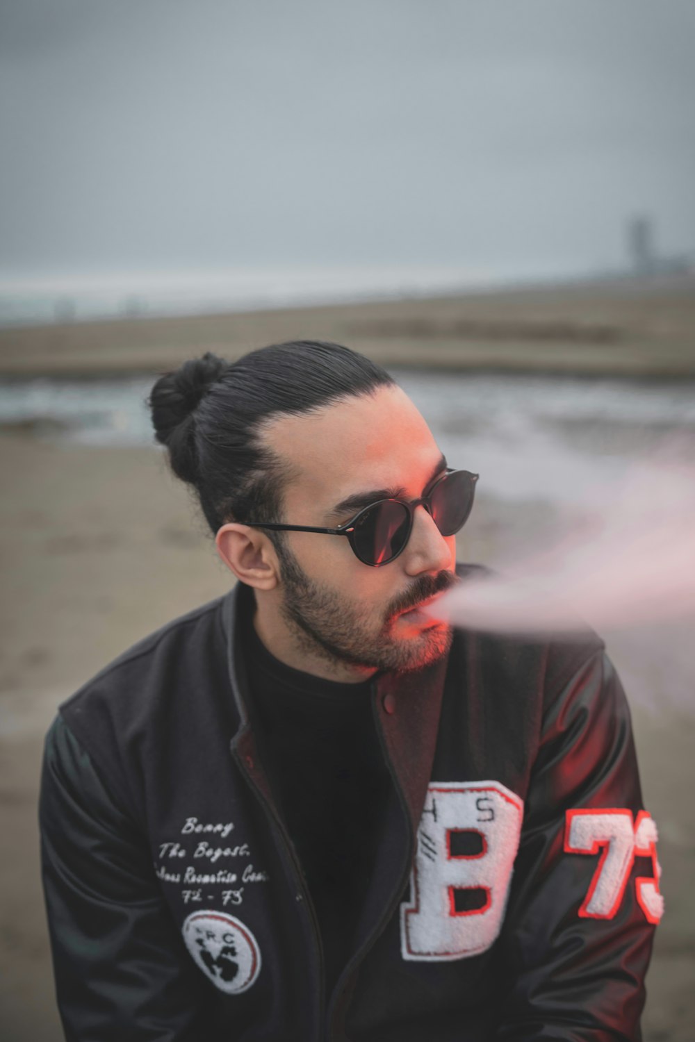 a man in a black jacket and sunglasses smoking a cigarette