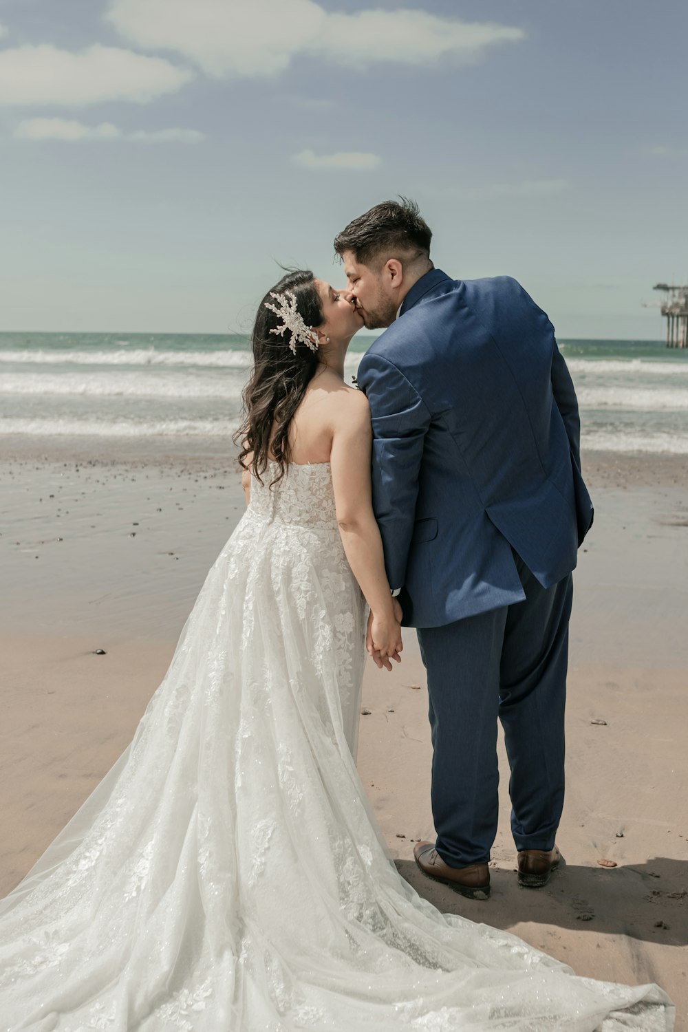 a bride and groom kissing on the beach