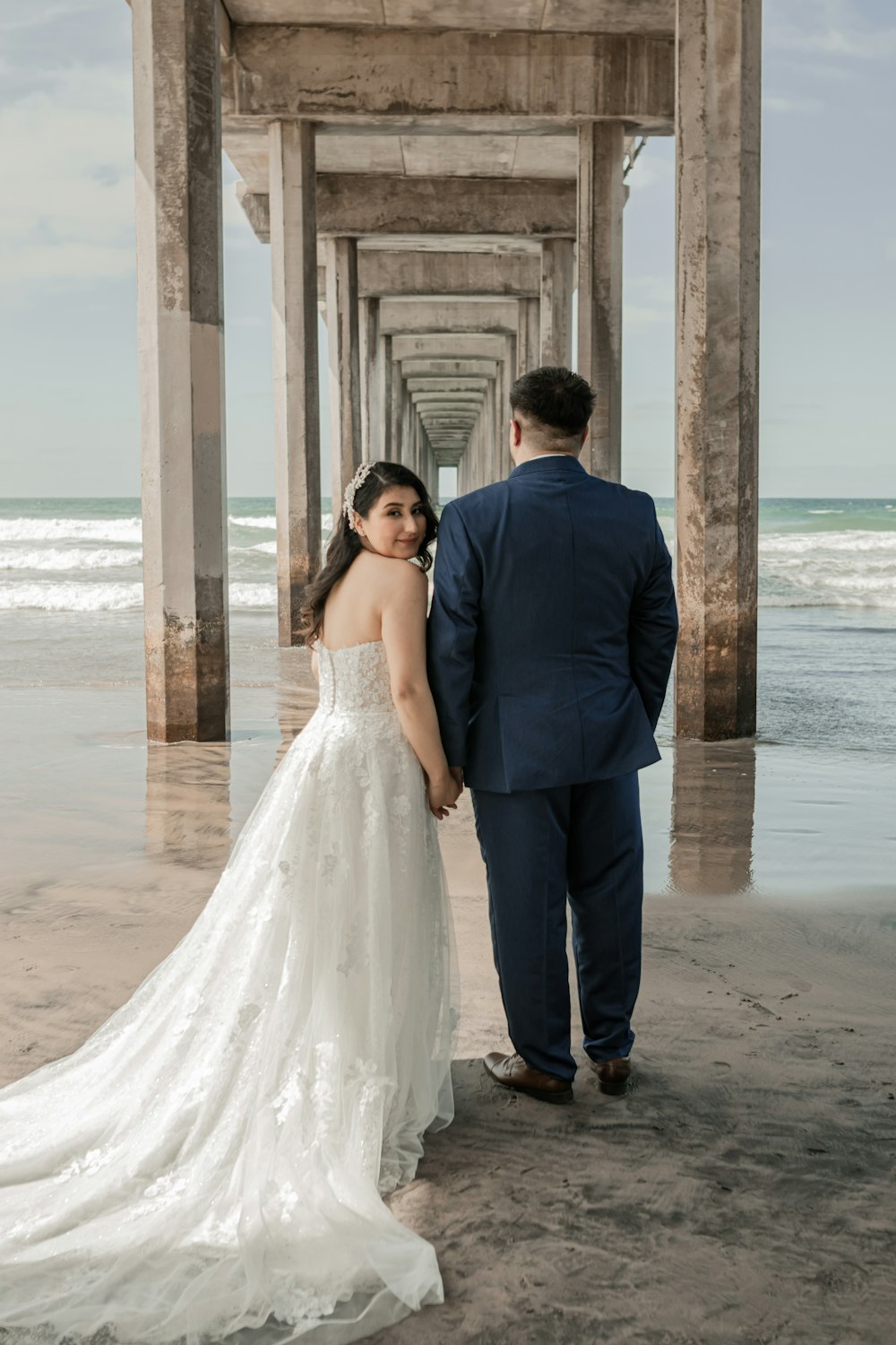 a bride and groom standing under a pier