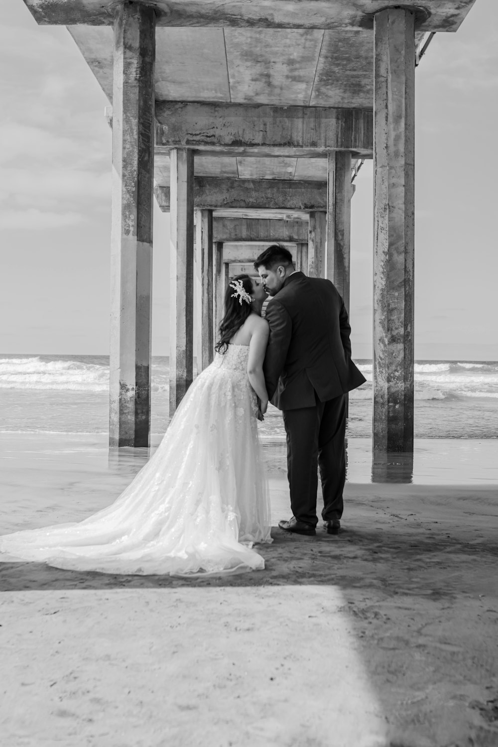 a bride and groom kissing under a pier