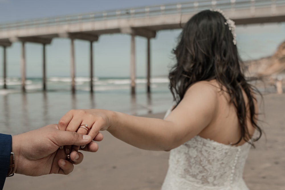 a bride and groom holding hands on the beach