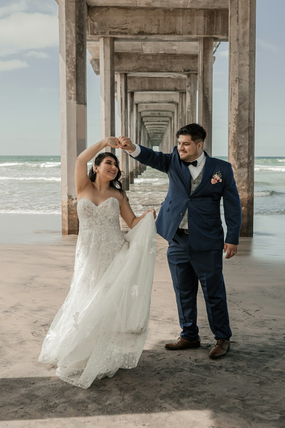 a bride and groom pose for a photo under a pier