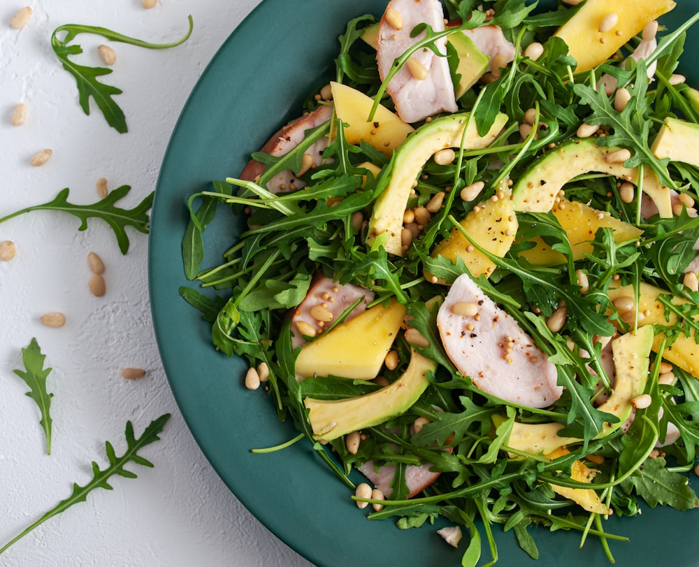 Un plato verde cubierto con una ensalada cubierta de aguacate