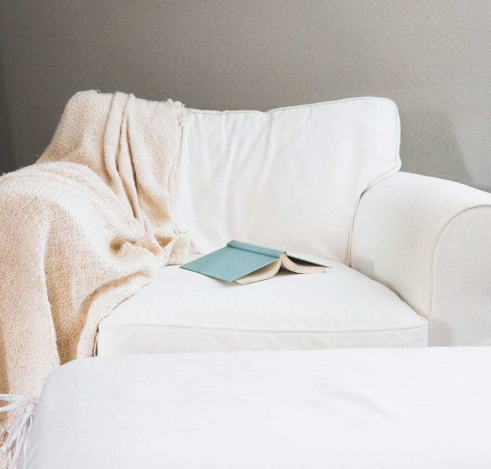 a white couch covered in a blanket and a book