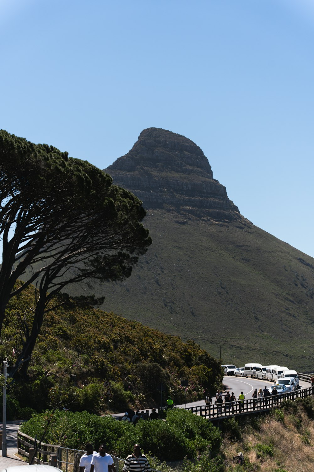 a group of people walking down a road next to a mountain