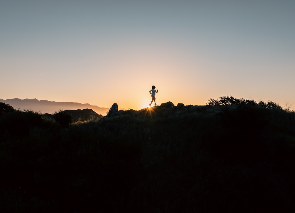 une personne debout au sommet d’une colline au coucher du soleil