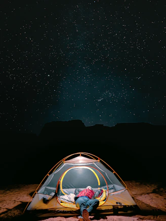 a man sitting inside of a tent under a night sky in tadrart rouge djanet algeria