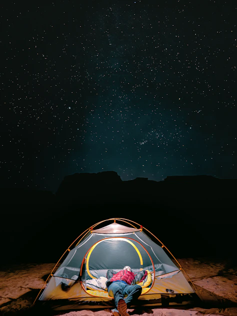 a man sitting inside of a tent under a night sky in tadrart rouge djanet algeria