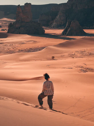Tourist exploring the rock formations and golden sands of Moul Naga in Tadrart Rouge, Algeria.