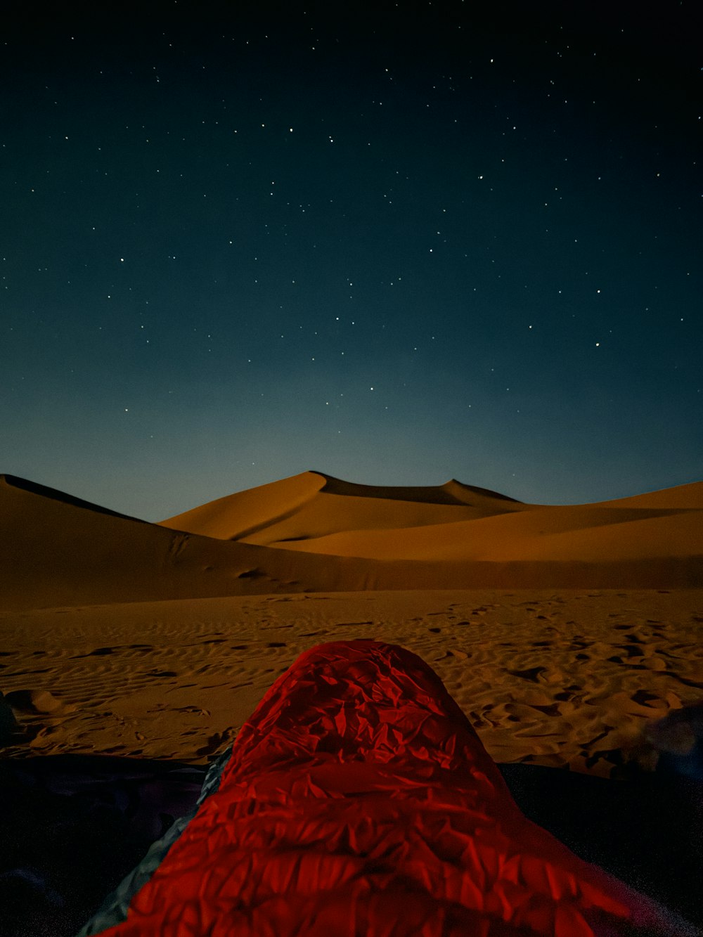 a red sleeping bag sitting on top of a sandy beach