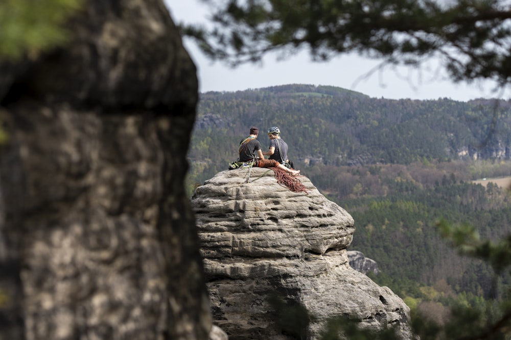 two people sitting on top of a large rock