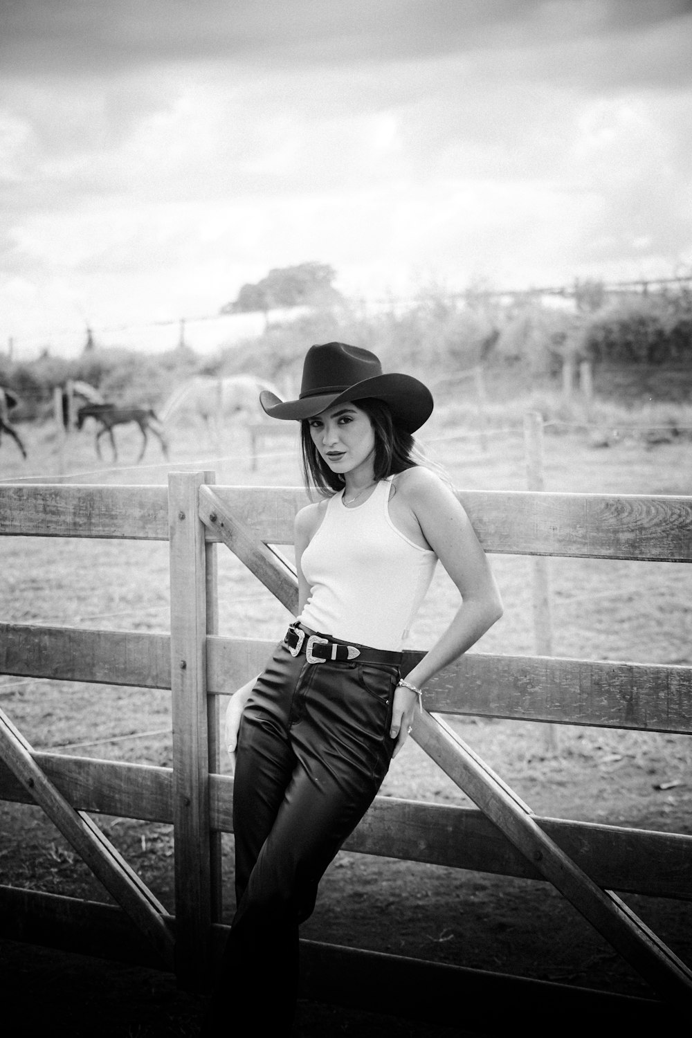 a woman in a cowboy hat leaning on a fence