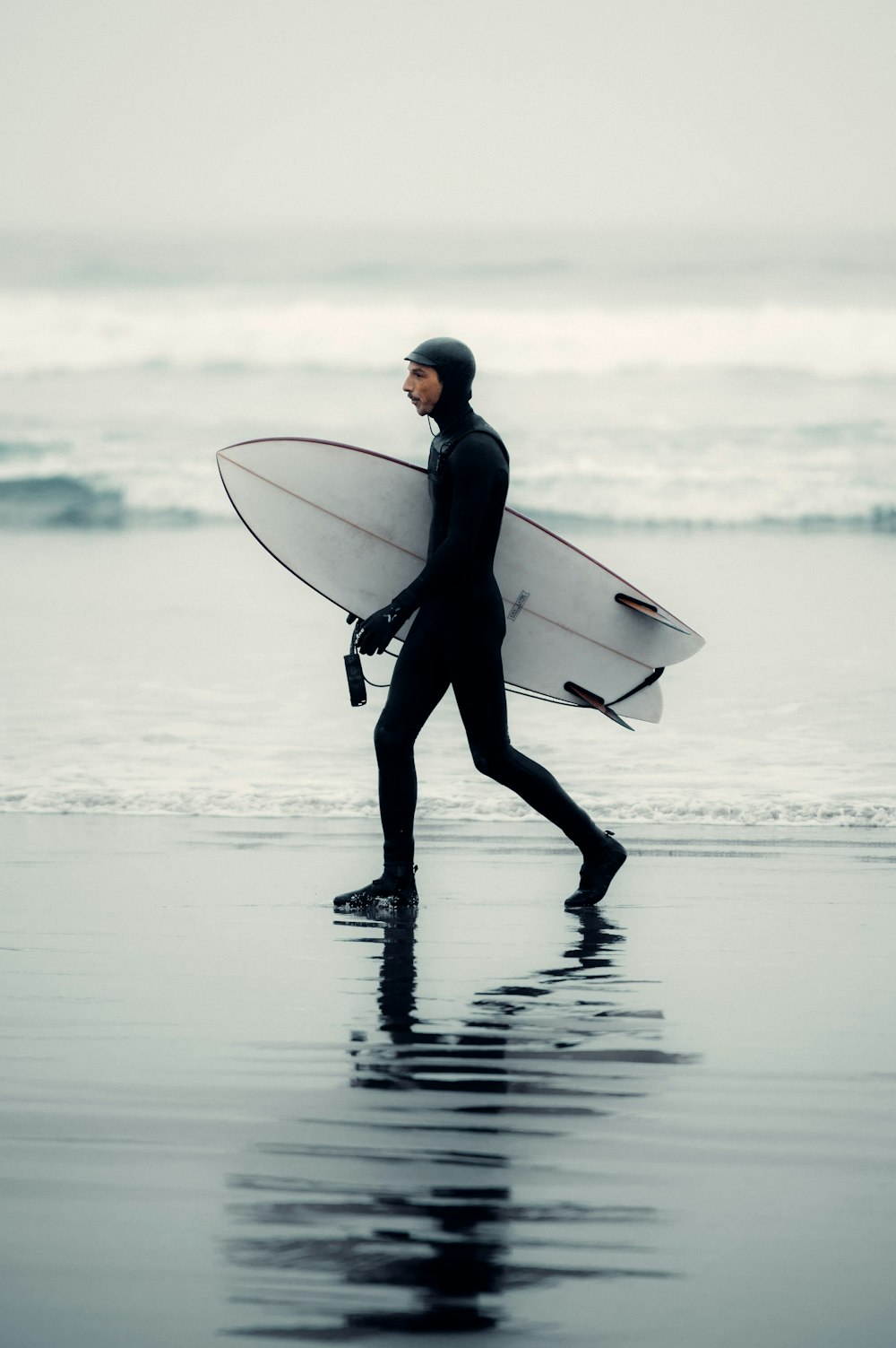 Un hombre con traje de neopreno cargando una tabla de surf